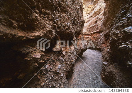 Narrow Slot Canyon Passage with Rugged Rock Walls and Sunlit Gravel Trail Narrow Slot Canyon Passage with Rugged Rock Walls and Sunlit Gravel Trail 142864588