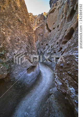 Narrow Slot Canyon Trail with Rugged Rock Walls and Natural Holes in Desert Landscape Narrow Slot Canyon Trail with Rugged Rock Walls and Natural Holes in Desert Landscape 142864592