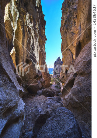 Narrow Desert Canyon with Sunlit Volcanic Rock Walls and Blue Sky Perspective Narrow Desert Canyon with Sunlit Volcanic Rock Walls and Blue Sky Perspective 142864637