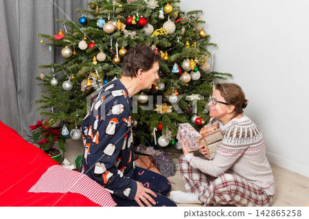 A couple sits near a Christmas tree on Christmas Day. They are exchanging gifts and enjoying the holiday spirit. The room has decorations and a festive atmosphere A couple sits near a Christmas tree on Christmas Day. They are exchanging gifts and enjoying the holiday spirit. The room has decorations and a festive atmosphere 142865258