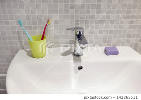 White ceramic sink with chrome faucet and plastic cup containing toothbrushes. White ceramic sink with chrome faucet and plastic cup containing toothbrushes. 142865511