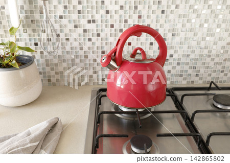 Red whistling kettle standing on stainless steel gas stove top.  142865802