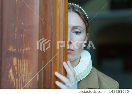 Woman peeking out from behind wooden door Woman peeking out from behind wooden door 142865950