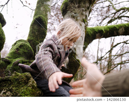 Child reaching out from mossy tree branch 142866130