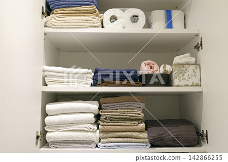 Organized bathroom cabinet shelves with folded linen stack. Organized bathroom cabinet shelves with folded linen stack. 142866255