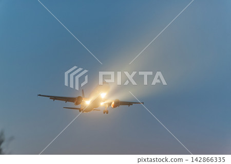 Airplane approaching at dusk with landing lights on Airplane approaching at dusk with landing lights on 142866335