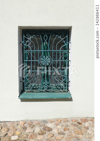 Aesthetic turquoise forged iron window bars cottagecore trend. Minimalist architectural lines on vintage white stucco wall facade with retro ornate security grill design background. Aesthetic turquoise forged iron window bars cottagecore trend. Minimalist architectural lines on vintage white stucco wall facade with retro ornate security grill design background. 142866411