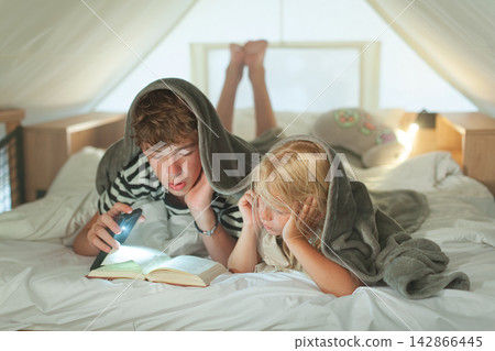 Children reading under blanket with flashlight Children reading under blanket with flashlight 142866445