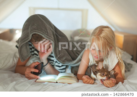Children reading under blanket with puppy 142866470