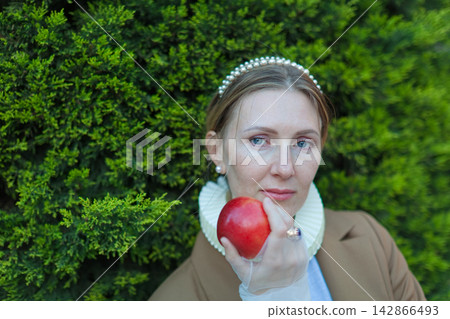 Woman holding red apple by green hedge Woman holding red apple by green hedge 142866493