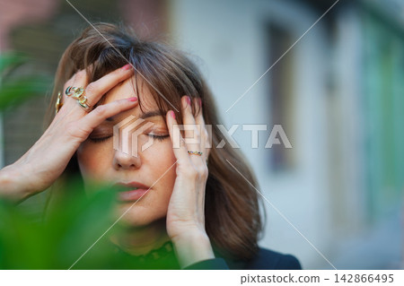 Woman with closed eyes holding head outdoors Woman with closed eyes holding head outdoors 142866495