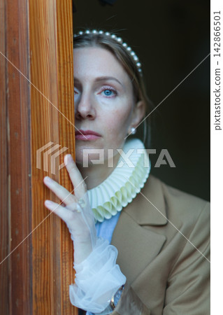Woman in vintage attire peering through door Woman in vintage attire peering through door 142866501