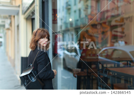 Woman in black coat looking at storefront window Woman in black coat looking at storefront window 142866545