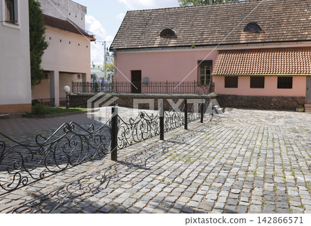 Historic courtyard of old town complex featuring pink baroque buildings with stone paved yard under blue sky. Ancient monument stands as significant piece of historical heritage and traditional archit Historic courtyard of old town complex featuring pink baroque buildings with stone paved yard under blue sky. Ancient monument stands as significant piece of historical heritage and traditional archit 142866571