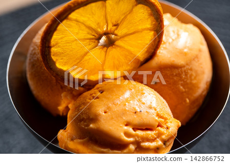 Orange sorbet scoops with dried orange slice in dark bowl Orange sorbet scoops with dried orange slice in dark bowl 142866752