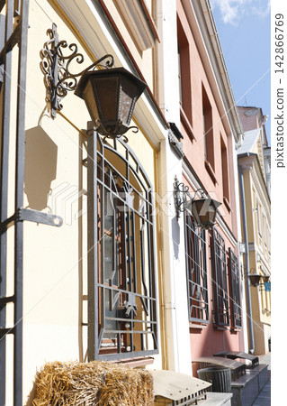 Forged iron lanterns window security bars photo. Vintage metal street lamps and geometric grills on colorful building facade wall. European old town street perspective architecture low angle view dayl Forged iron lanterns window security bars photo. Vintage metal street lamps and geometric grills on colorful building facade wall. European old town street perspective architecture low angle view dayl 142866769