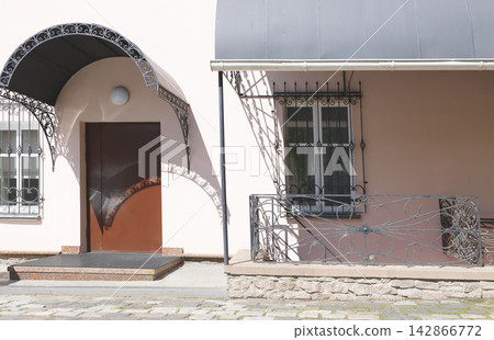 Forged iron railing window bars entrance. Vintage metal porch awning and decorative security grill cast sharp shadows on pink building facade wall. Old town courtyard architectural details background. 142866772