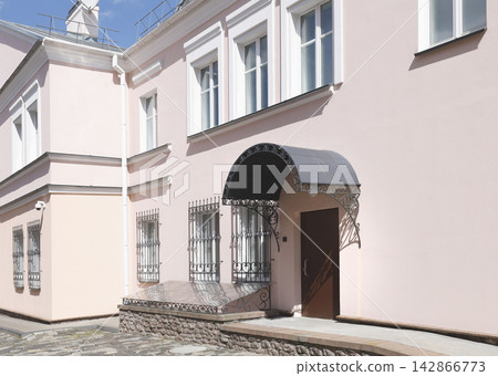 Classical European architecture old town mansion building exterior. Traditional classic house facade with pastel pink walls white window frames forged iron entrance canopy Classical European architecture old town mansion building exterior. Traditional classic house facade with pastel pink walls white window frames forged iron entrance canopy 142866773