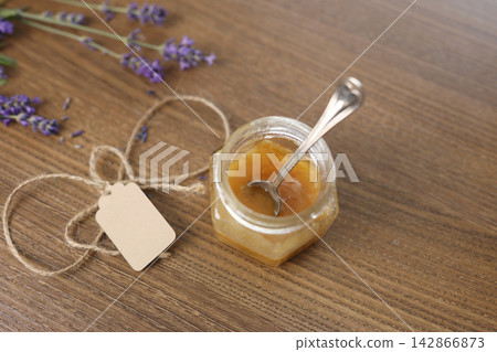Small honey glass jar string twine tag spoon inside wooden table top view. Fresh purple lavender flower blooming bouquet bunch side background. Natural organic food product copy space template. Small honey glass jar string twine tag spoon inside wooden table top view. Fresh purple lavender flower blooming bouquet bunch side background. Natural organic food product copy space template. 142866873