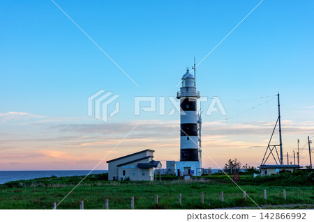 The Nyudozaki Lighthouse stands in the early morning at Nyudozaki on the Oga Peninsula in Akita Prefecture. A view of the lighthouse against the morning sky. The Nyudozaki Lighthouse stands in the early morning at Nyudozaki on the Oga Peninsula in Akita Prefecture. A view of the lighthouse against the morning sky. 142866992