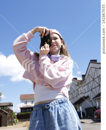 Trendy gen alpha girl taking photo with vintage camera outdoors. Cool tween in pink hoodie holding retro film cam against blue sky. Youth hobby and street fashion lifestyle on bright summer day. Trendy gen alpha girl taking photo with vintage camera outdoors. Cool tween in pink hoodie holding retro film cam against blue sky. Youth hobby and street fashion lifestyle on bright summer day. 142867035