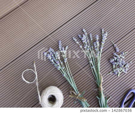 Lavender stems scissors twine ball on wooden background process of making bouquets. Dried organic lavender preparation workspace flat lay view composition. Handcraft hobby workspace with purple flower Lavender stems scissors twine ball on wooden background process of making bouquets. Dried organic lavender preparation workspace flat lay view composition. Handcraft hobby workspace with purple flower 142867036