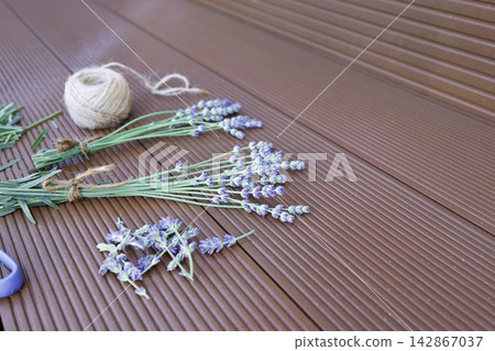 Lavender stems scissors twine ball on wooden background process of making bouquets. Dried organic lavender preparation workspace flat lay view composition. Handcraft hobby workspace with purple flower 142867037