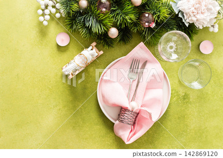 Top view of an elegant Christmas table with an empty plate, folded pink napkin and cutlery on a vibrant green background. Spruse branches and pink tree decorations add seasonal charm Top view of an elegant Christmas table with an empty plate, folded pink napkin and cutlery on a vibrant green background. Spruse branches and pink tree decorations add seasonal charm 142869120