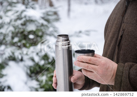 Man holding stainless steel thermos cup outdoors in winter forest Man holding stainless steel thermos cup outdoors in winter forest 142869752