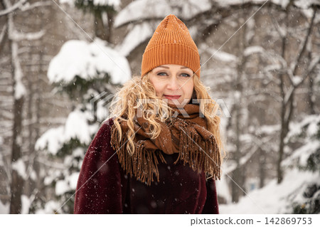 Smiling woman in winter coat standing outdoors during snowfall Smiling woman in winter coat standing outdoors during snowfall 142869753