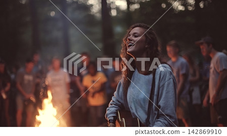 Woman singing and playing guitar at outdoor campfire gathering Woman singing and playing guitar at outdoor campfire gathering 142869910