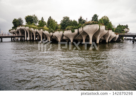 Close up of Little Island's unique concrete tulip shaped pillars rising above the Hudson River in Manhattan. Lush greenery and modern architecture create a striking urban waterfront landmark. Close up of Little Island's unique concrete tulip shaped pillars rising above the Hudson River in Manhattan. Lush greenery and modern architecture create a striking urban waterfront landmark. 142870298