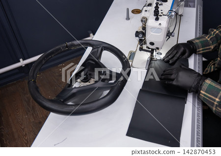 A seamstress in a workshop makes a new leather cover for a car steering wheel. A seamstress in a workshop makes a new leather cover for a car steering wheel. 142870453