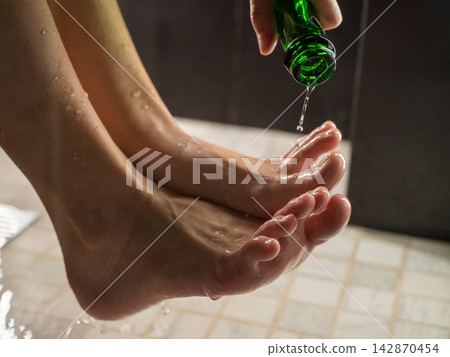 Foot fetish. A woman pours beer from a bottle onto her toes. Foot fetish. A woman pours beer from a bottle onto her toes. 142870454