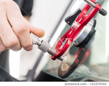A technician injects resin into a windshield crack.  142870504