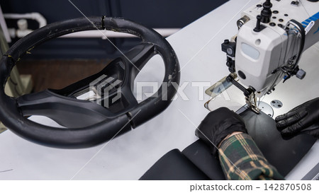 A seamstress in a workshop makes a new leather cover for a car steering wheel. A seamstress in a workshop makes a new leather cover for a car steering wheel. 142870508