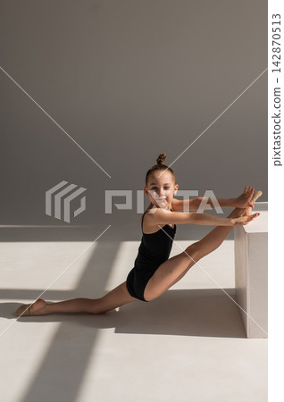 Little Caucasian girl gymnast in a black leotard posing on a white background. Little Caucasian girl gymnast in a black leotard posing on a white background. 142870513