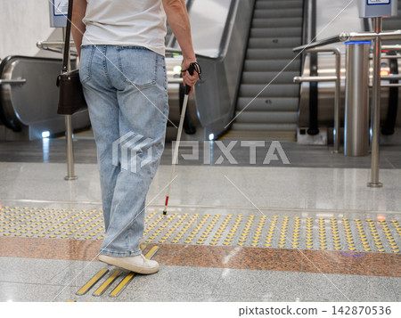 A blind woman in the metro near an escalator follows tactile navigation tiles. A blind woman in the metro near an escalator follows tactile navigation tiles. 142870536