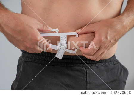 A man measures the amount of subcutaneous fat on his stomach using a caliper. A man measures the amount of subcutaneous fat on his stomach using a caliper. 142870608