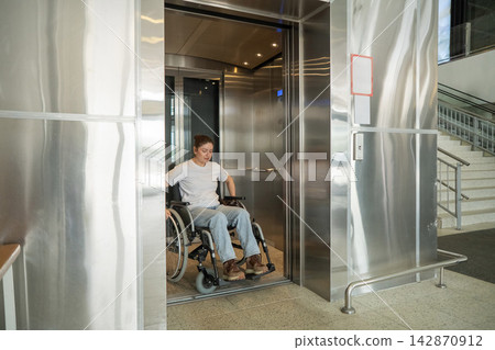 A Caucasian woman in a wheelchair uses an elevator. A Caucasian woman in a wheelchair uses an elevator. 142870912