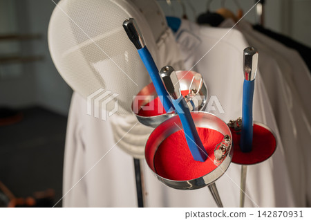 Fencing uniforms and masks hang on hangers. No people. Fencing uniforms and masks hang on hangers. No people. 142870931