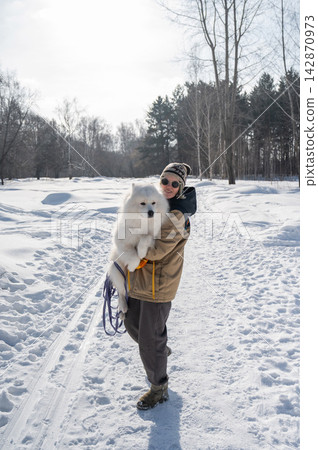 Smiling woman holding fluffy samoyed dog in snowy winter park. Smiling woman holding fluffy samoyed dog in snowy winter park. 142870973