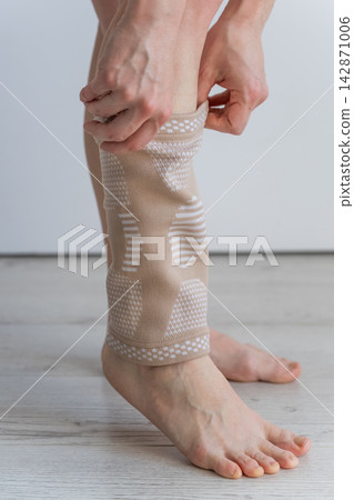 A Caucasian woman suffers from knee pain and wears a supportive elastic knee brace. A Caucasian woman suffers from knee pain and wears a supportive elastic knee brace. 142871006
