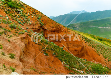 Eroded Red Clay Hillside with Green Vegetation in Kyrgyzstan 142871136