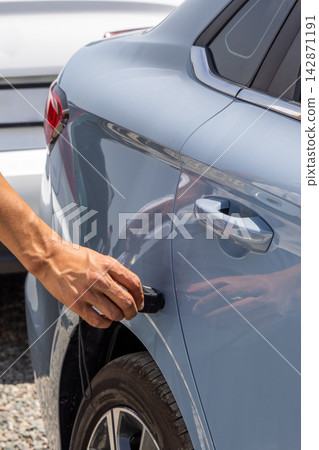 Hand Using Electronic Paint Thickness Measuring Device on Light Blue Sedan 142871191