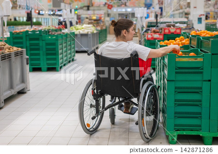A Caucasian woman in a wheelchair buys fruit at a supermarket. A Caucasian woman in a wheelchair buys fruit at a supermarket. 142871286