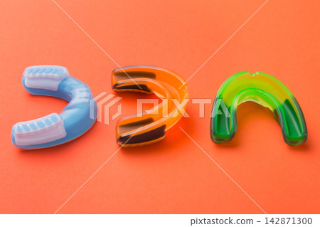 Three colorful silicone mouthguards for sports protection placed on orange background Three colorful silicone mouthguards for sports protection placed on orange background 142871300