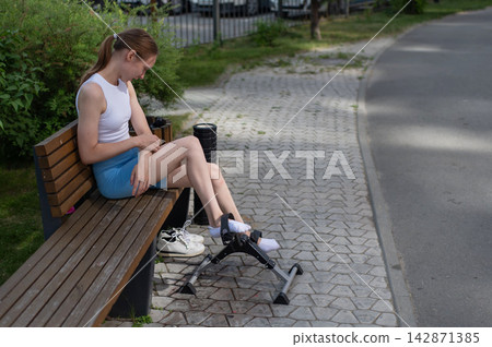 A woman uses Pedal Exercise Machine for self-rehabilitation outdoors. A woman uses Pedal Exercise Machine for self-rehabilitation outdoors. 142871385