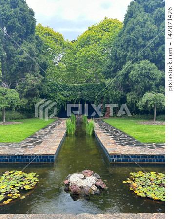 Symmetrical garden with pond, grotto, and lush green trees Symmetrical garden with pond, grotto, and lush green trees 142871426