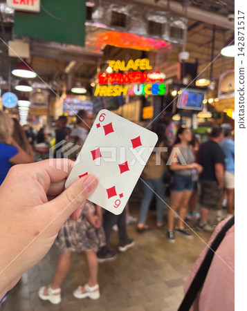 Holding the six of diamonds playing card in a busy food market Holding the six of diamonds playing card in a busy food market 142871517
